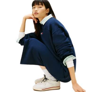 Frau in blauem Oversize-Pullover und weißem Hemd, hockend, trägt weiße Schuhe und lange weiße Socken.