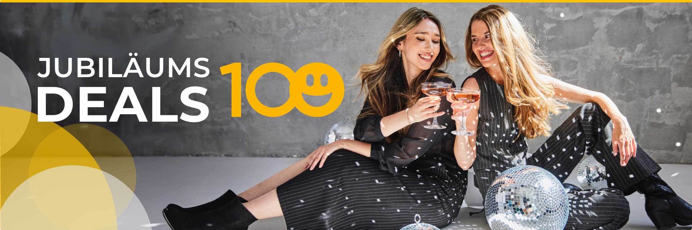 Jubiläums-Deals BAUR 100 - zwei Frauen in schwarzen Outfits stoßen mit Sekt an, es liegen Diskokugeln auf dem Boden