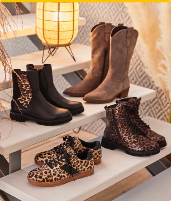 Vier Paar Schuhe auf einem Regal – braune Stiefeletten, schwarze Stiefeletten, Leopardenmuster-Boots und Leopardenmuster-Sneakers