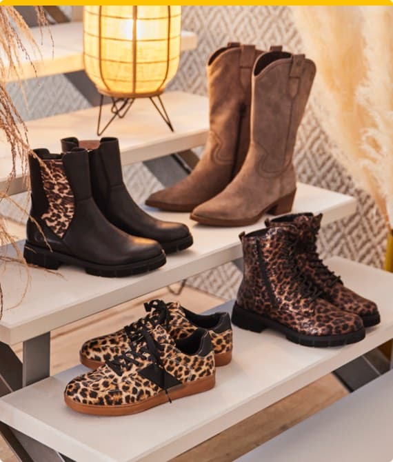Vier Paar Schuhe in Leopardenoptik – schwarze Stiefel, braune Stiefel, schwarze Boots und Sneaker auf weißen Regalen