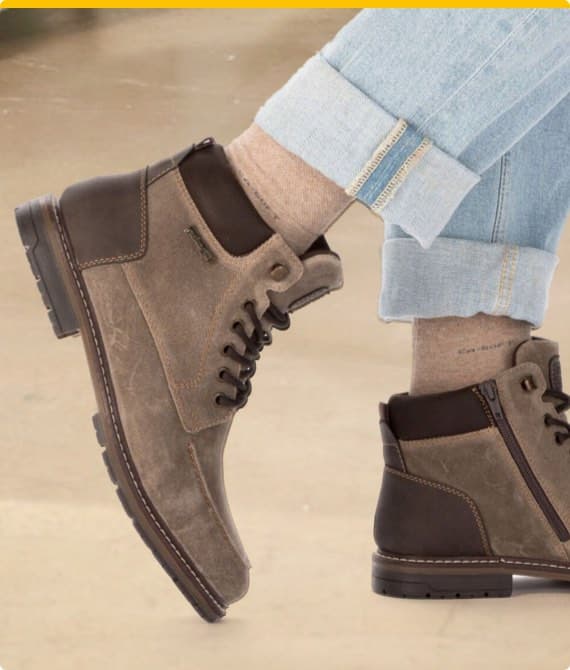 Zwei Füße in braunen Herren-Schnürstiefeln und hochgekrempelten hellblauen Jeans, beige Socken sichtbar