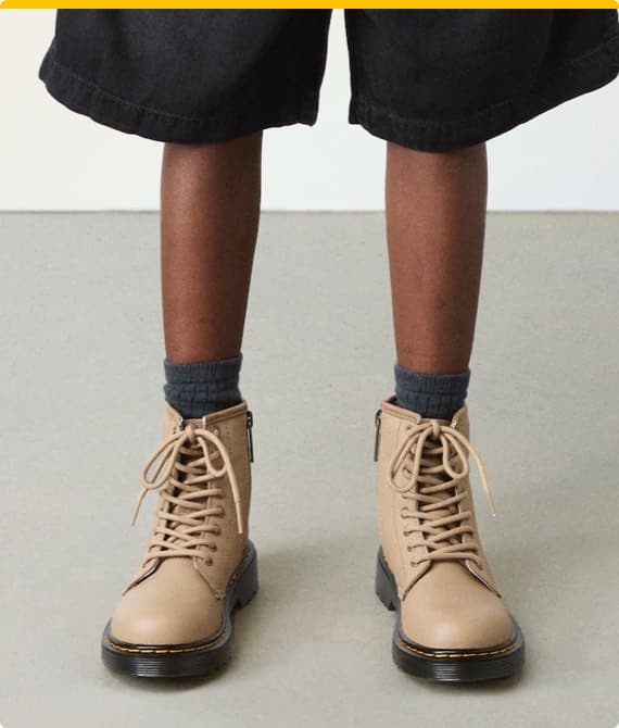 Beine eines Kindes in schwarzen Shorts und grauen Socken, die beige Stiefel mit Schnürung trägt