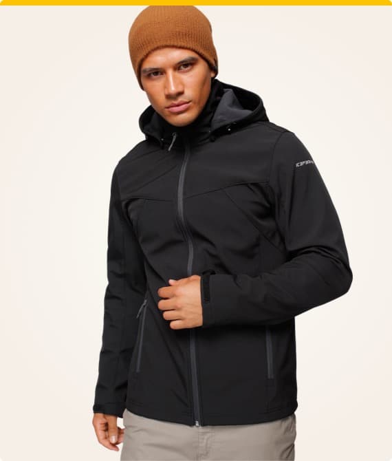 Mann trägt schwarze Kapuzenjacke und beige Hose, Mütze in Orange