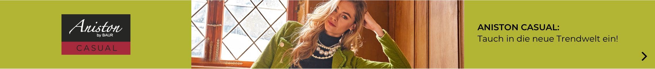 ANISTON CASUAL: Tauch in die neue Trendwelt ein! Frau in grünem Pullover vor Fenster mit Holzrahmen und Glasornamenten.
