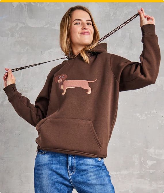 Person in braunem Hoodie mit Hundemotiv und blauer Jeans hält Kapuzen-Schnur mit "DOG LOVER" Schriftzug.