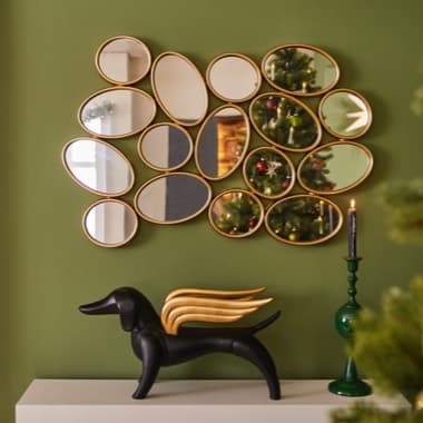 Spiegel mit goldenen Umrandungen an grüner Wand, Weihnachtsbaum im Hintergrund, schwarze Hundeskulptur mit Flügeln auf weißem Regal
