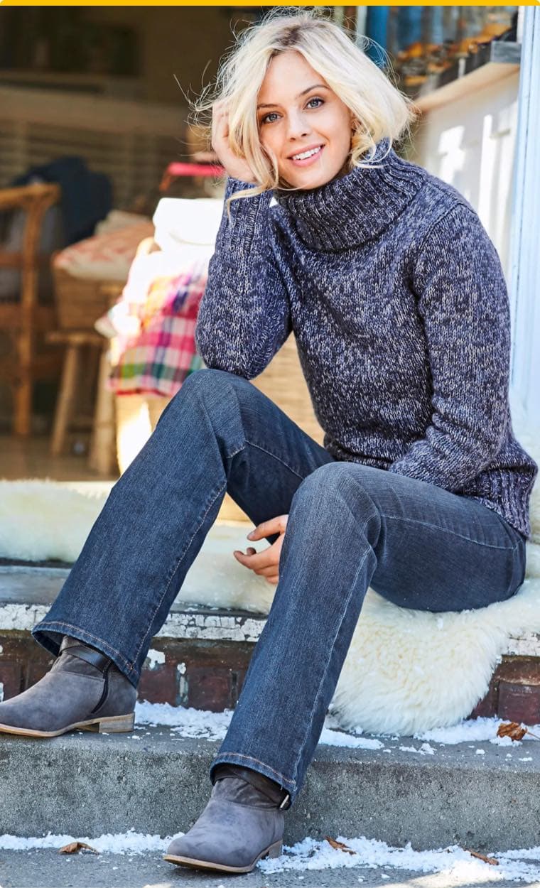 Person in blauem Pullover und Jeans sitzt draußen auf einer Treppe, stützt Kopf auf Hand und trägt graue Stiefeletten