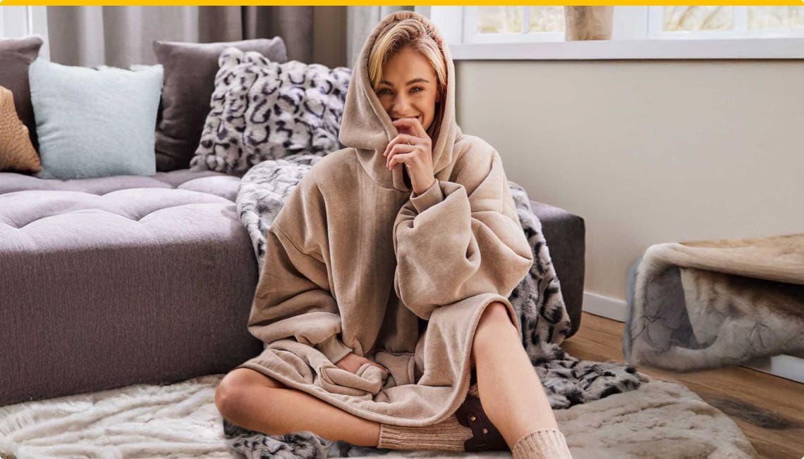 Person sitzt in einem gemütlichen Raum auf einem Teppich, trägt einen beigen Hoodie und Wollsocken, Gesicht ist verschwommen