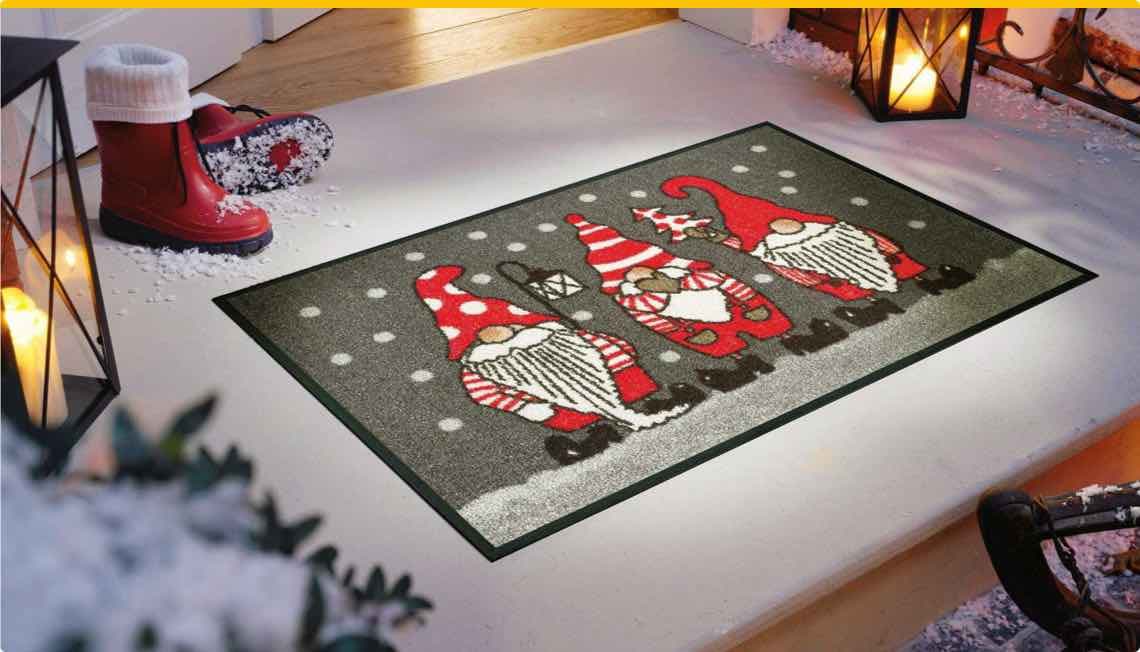 Fußmatte mit drei Weihnachtswichteln in rot-weiß, Schnee, Laterne, rote Stiefel, Laterne und Schneeflocken im Hintergrund