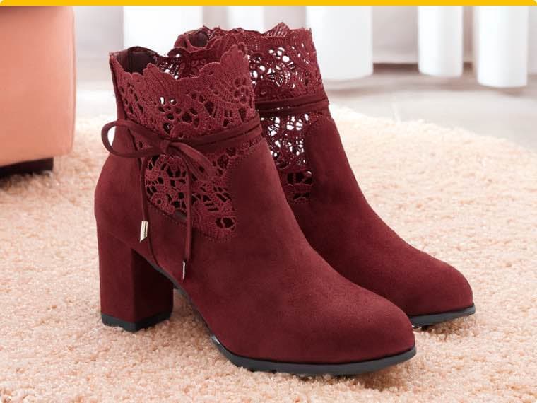 Weinrote Stiefeletten mit Blockabsatz und Spitzenmuster, auf hellem Teppich vor einem rosa Sessel und weißen Vorhängen.