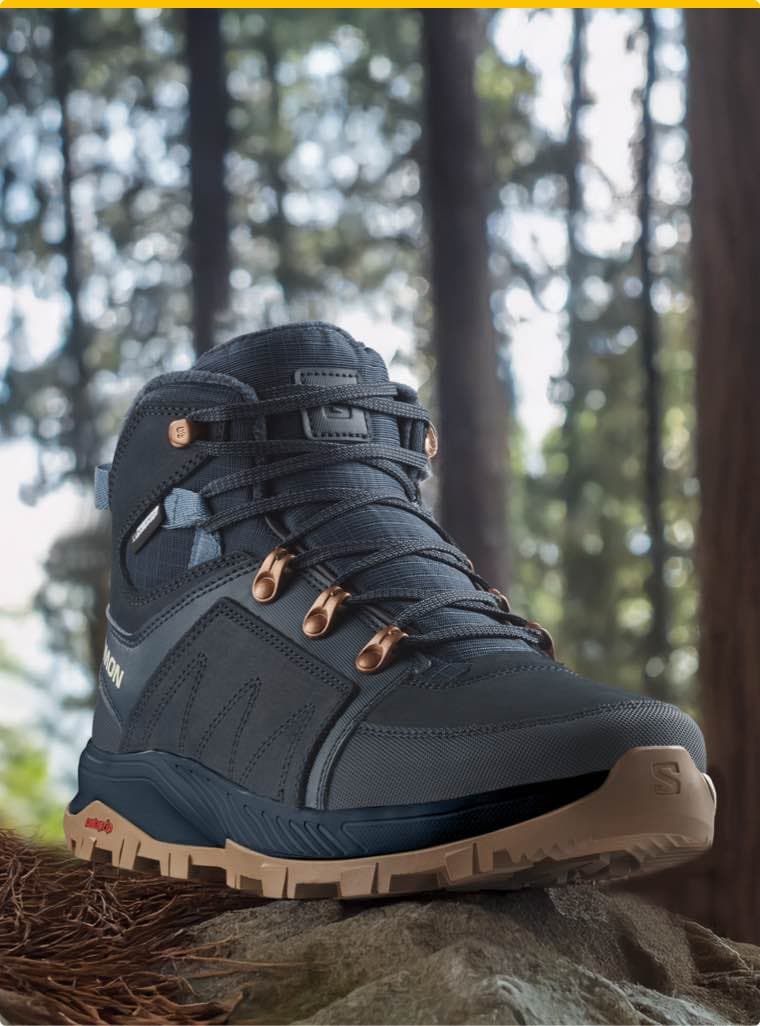 Dunkelblauer Wanderschuh mit beige Sohle und Schnürsenkeln, präsentiert im Wald auf einem Felsen.