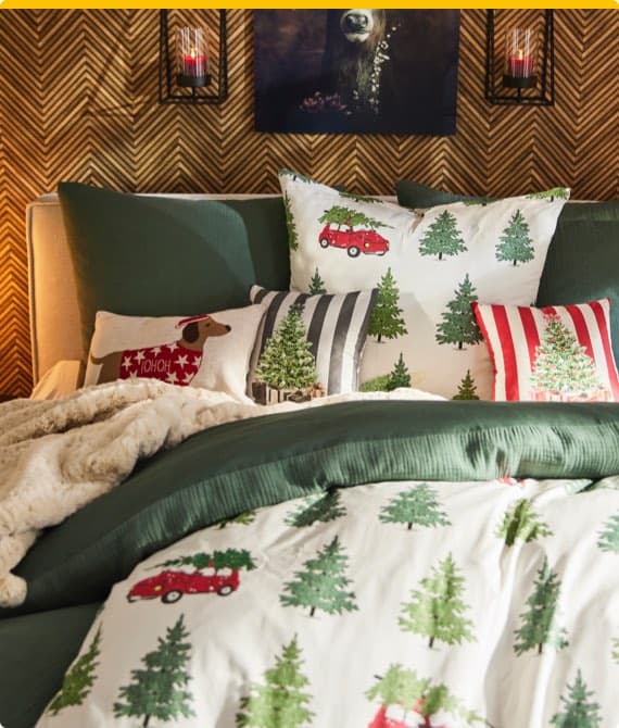 Bett mit Weihnachtsbettwäsche und Kissen, die Bäume und einen Hund mit "HoHoHo" zeigen, weiche Decke und gemütliches Zimmer