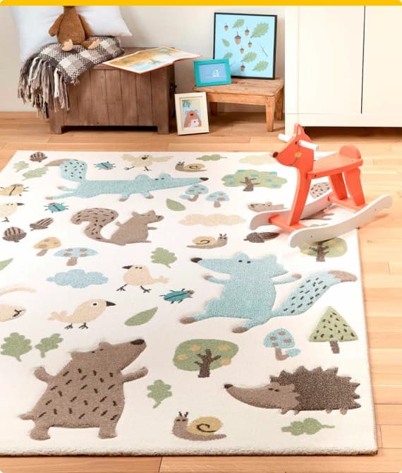 Kinderzimmer mit Teppich, der Waldtiere zeigt, und rotem Schaukelpferd. Im Hintergrund ein Holzhocker mit Deko und Kissen.