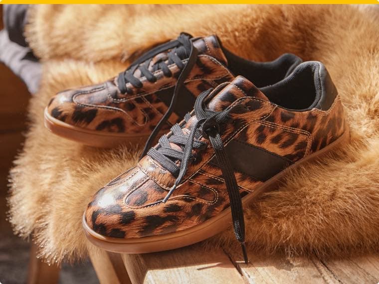 Leopard gemusterte Sneakers mit schwarzen Schnürsenkeln auf einem braunen Fell drapiert
