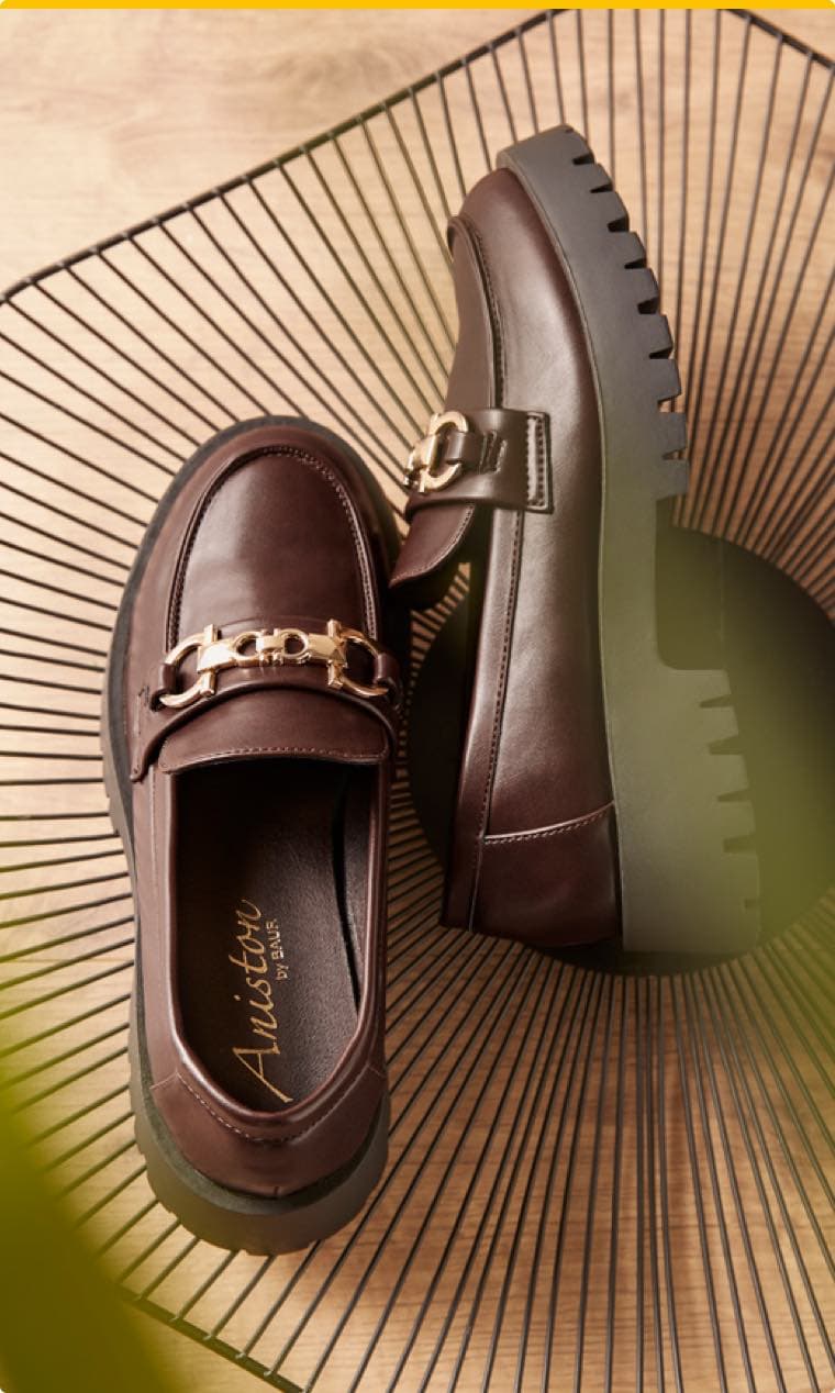 Aniston by Baur – braune Loafer mit goldener Schnalle, auf dekorativem Hintergrund liegend