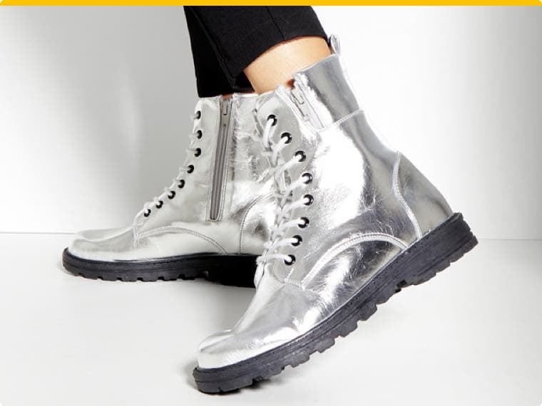 Silberne Schnürstiefel mit schwarzer Sohle und Reißverschluss, getragen von Person in schwarzen Hosen.