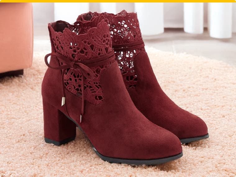 Weinrote Stiefeletten mit Blockabsatz und Spitzenmuster, auf hellem Teppich vor einem rosa Sessel und weißen Vorhängen.