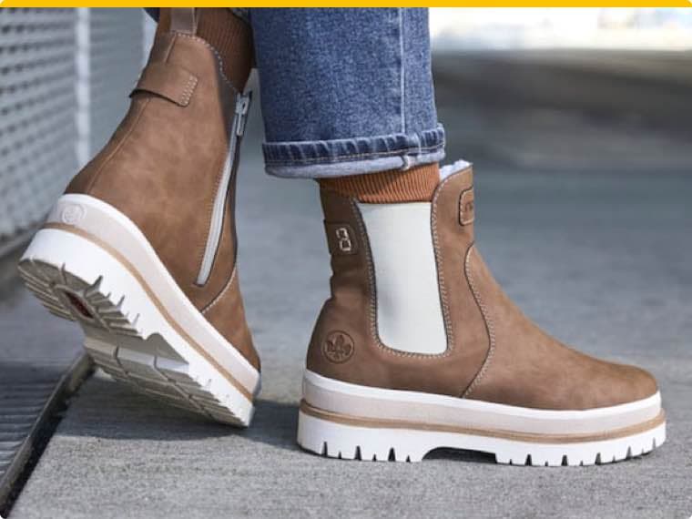 Braune Stiefeletten mit weißen Sohlen und seitlichen Reißverschlüssen, getragen zu hochgekrempelten Jeans auf Gehweg