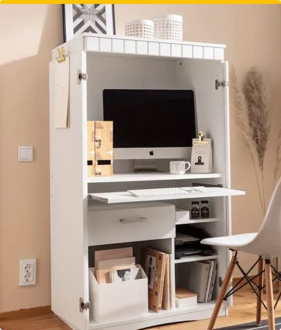 Aufgeklappter weißer Sekretär mit Computer, Aktenordnern und Büroartikeln, daneben weißer Stuhl vor hellbeiger Wand.