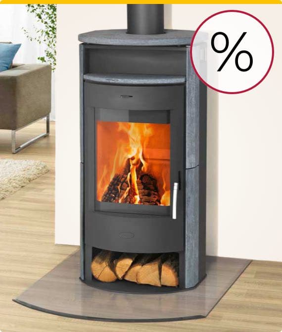 Prozentzeichen – Schwarzer Kaminofen mit brennendem Feuer, Holzscheite im unteren Fach, Wohnzimmer im Hintergrund