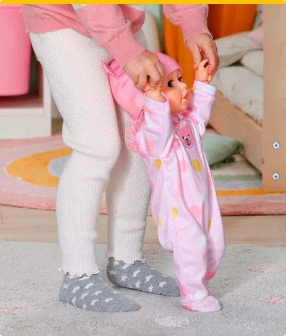 Kind spielt mit einer Puppe, die einen rosa Schlafanzug mit Punkten trägt