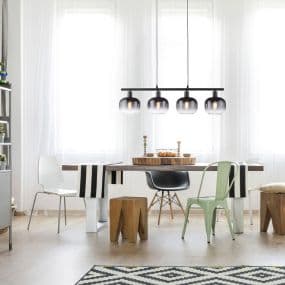 Esszimmer mit weißem Tisch, gemischten Stühlen und hängender Lampenleiste vor drei Fenstern.