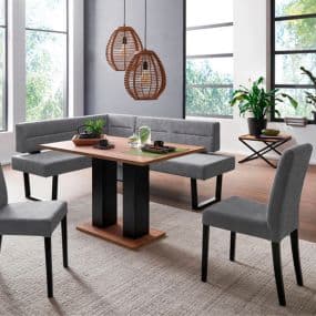 Eckbankgruppe mit grauen Sitzpolstern und Holztisch, zwei Lampen hängen von der Decke, Pflanzen im Hintergrund