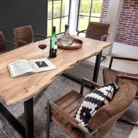 Holztisch mit zwei Weinflaschen, einem Glas und einem geöffneten Buch, umgeben von vier braunen Stühlen in modernem Raum.