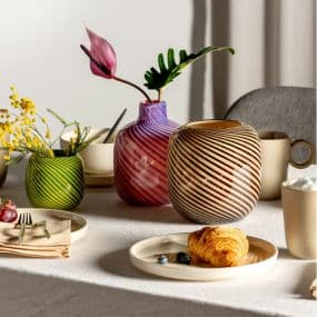 Frühstückstisch mit gestreiften Vasen, Croissant und Blumenarrangements in bunten Vasen