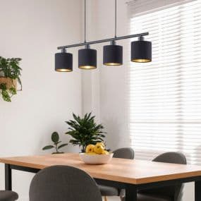 Esszimmer mit Holz-Tisch, Obstschale, grauen Stühlen und schwarzer Deckenleuchte vor Fenster mit Lamellen. Pflanzen im Hintergrund.