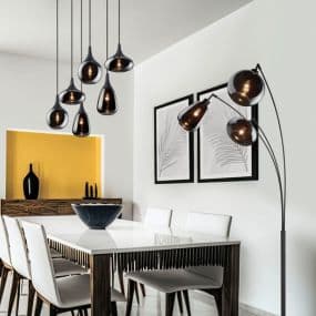 Moderne Esszimmerbeleuchtung mit schwarzen Pendelleuchten und Stehlampe, weißer Tisch und Stühle, Wandkunst mit Pflanzenmotiv.