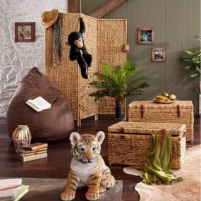 Wohnzimmer mit Korbmöbeln, Tigerfigur, braunem Sitzsack, Hängelampe, Pflanze und Stoffaffe an einem Raumteiler