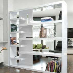 Weißes Regal mit Büchern und Deko, steht im modernen Wohnzimmer mit Holzboden und grauem Sofa.