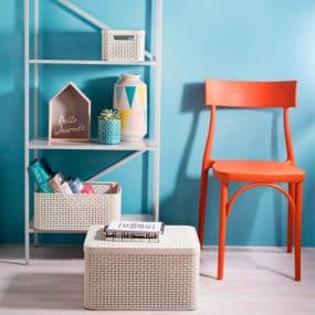 Hellblaues Zimmer mit orangem Stuhl, weißem Regal und Körben, dekoriert mit Büchern und Vasen.