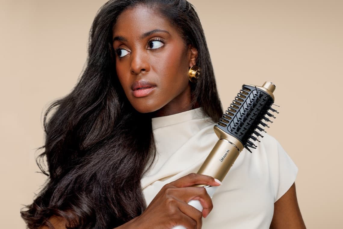 Frau mit langen, dunklen Haaren hält eine goldene Rundbürste.