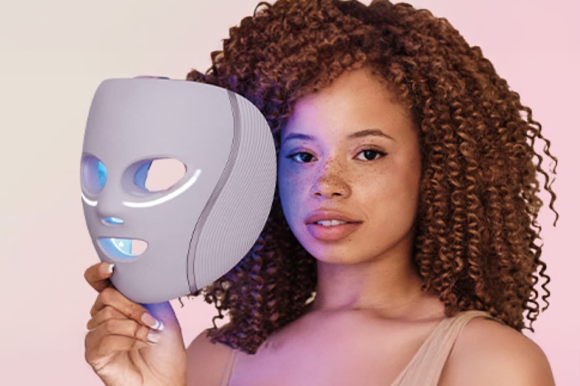 Frau mit lockigem Haar hält einen grauen Gegenstand in der Hand vor ihrem Gesicht