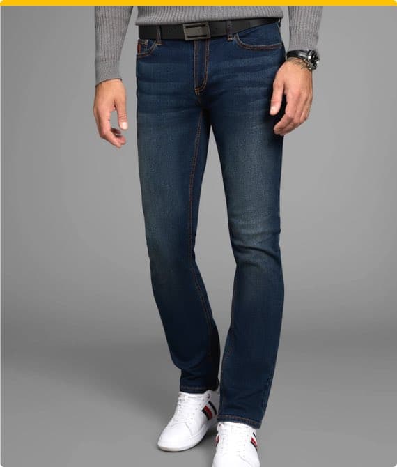 Mann in dunkelblauer Jeans und grauem Pullover, trägt weiße Sneakers mit roten und schwarzen Streifen, grauer Hintergrund