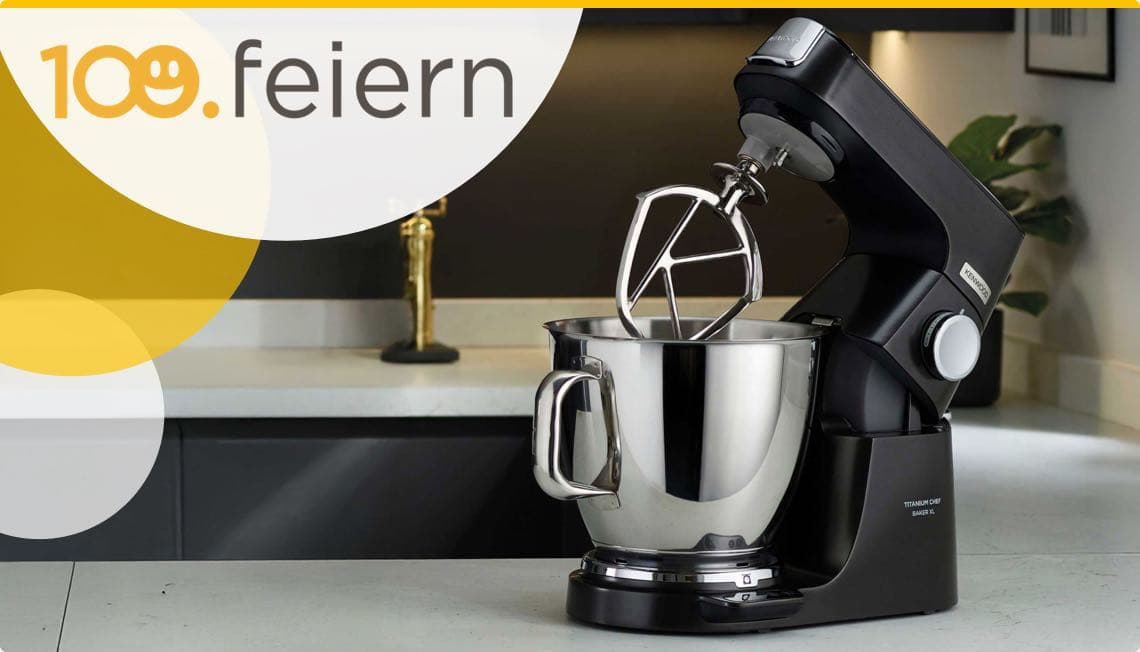 100. feiern – Schwarze Küchenmaschine mit Edelstahlrührschüssel und Rührbesen auf Küchenarbeitsplatte