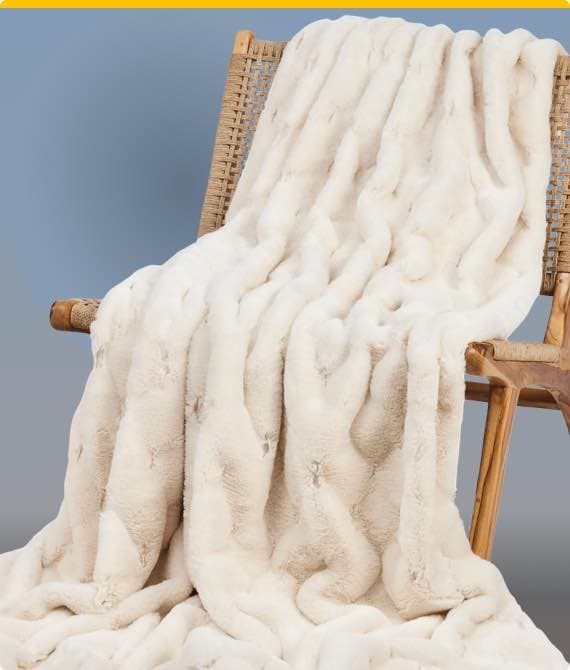 Weiche cremefarbene Decke liegt drapiert über einem Holzstuhl mit geflochtener Rückenlehne