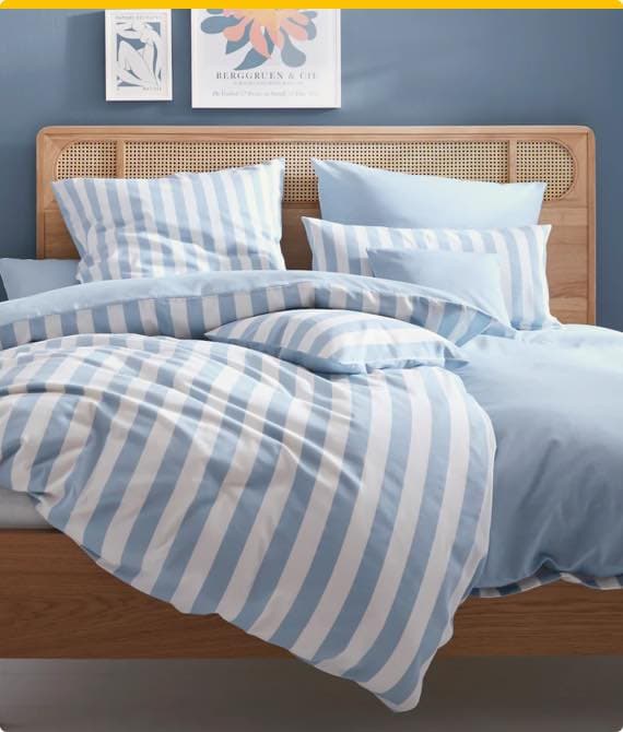 Bett mit blau-weiß gestreifter Bettwäsche, mehrere Kissen, Holz-Kopfteil, blaue Wand mit zwei Bildern
