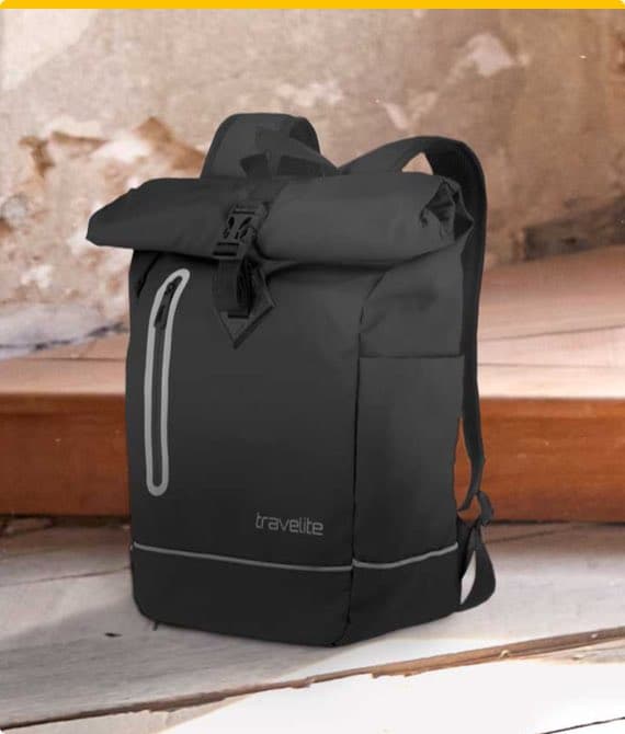 Schwarzer Travelite-Rucksack mit Rolltop-Verschluss und Reißverschlusstasche auf Holzbank vor gemauerter Wand