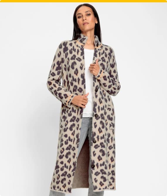 Frau trägt langen, offenen Mantel mit Leopardenmuster, weißes Oberteil und graue Hose.