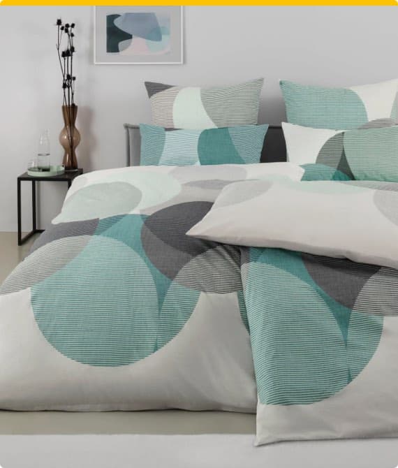 Bettwäsche mit geometrischen Kreisen in Blau-, Grau- und Weißtönen auf einem Bett in modernem Schlafzimmer.
