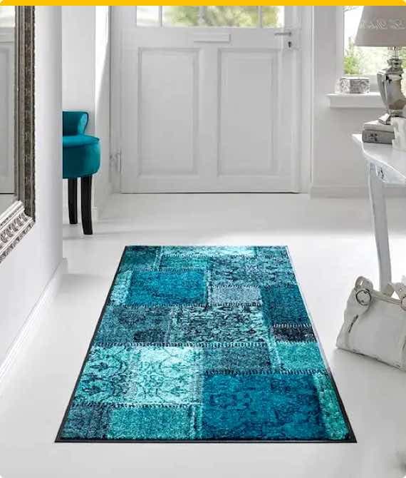 Türmatte in Blau mit Patchwork-Design liegt in hellem Flur vor weißer Tür.