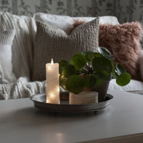 Wohnzimmerdekoration mit Kerze, Pflanze und Kissen auf Sofa im Hintergrund