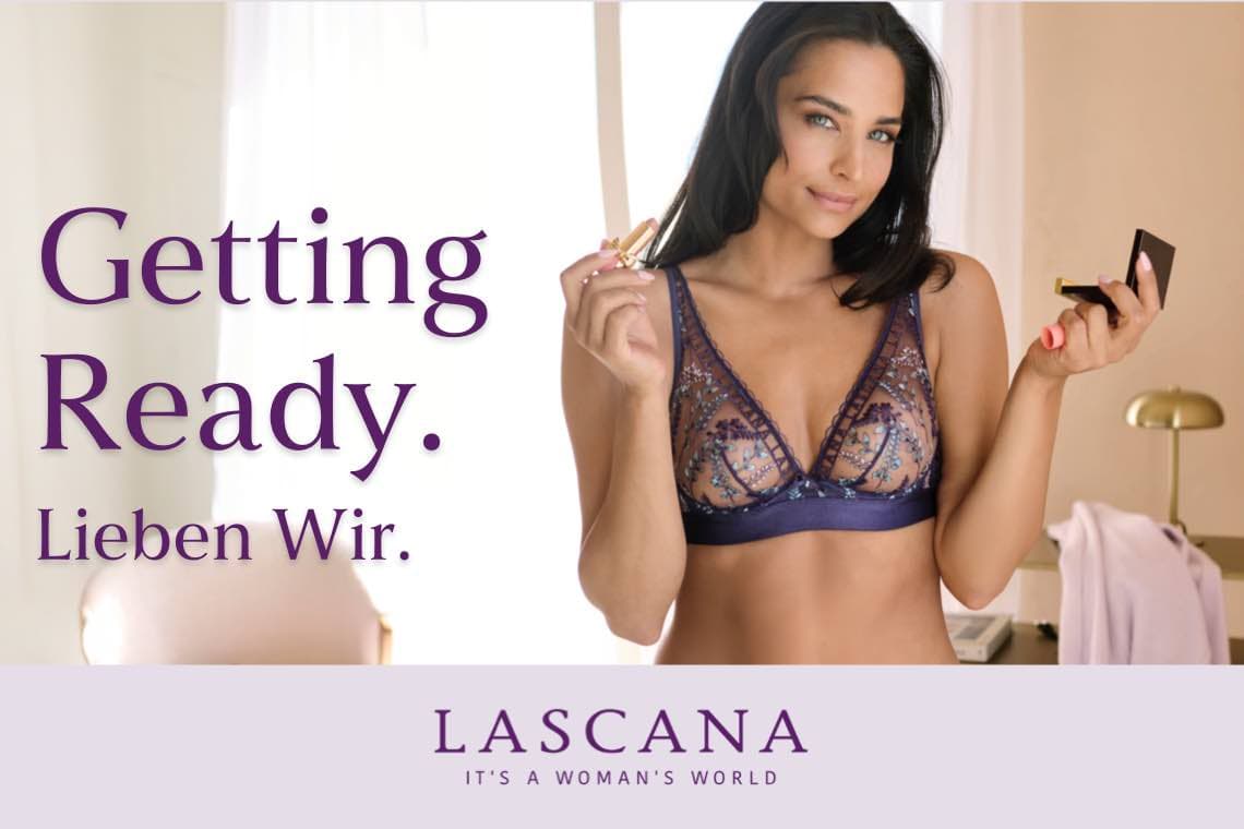 Getting Ready. Lieben Wir. Frau in lila Spitzen-BH trägt Lippenstift auf und hält einen Spiegel. LASCANA - It's a woman's world.