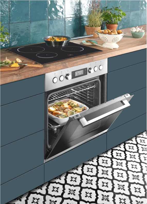 Moderne Küche mit offenem Backofen, darin Auflaufform. Auf der Arbeitsplatte stehen Pfanne und Schüsseln mit Zutaten.