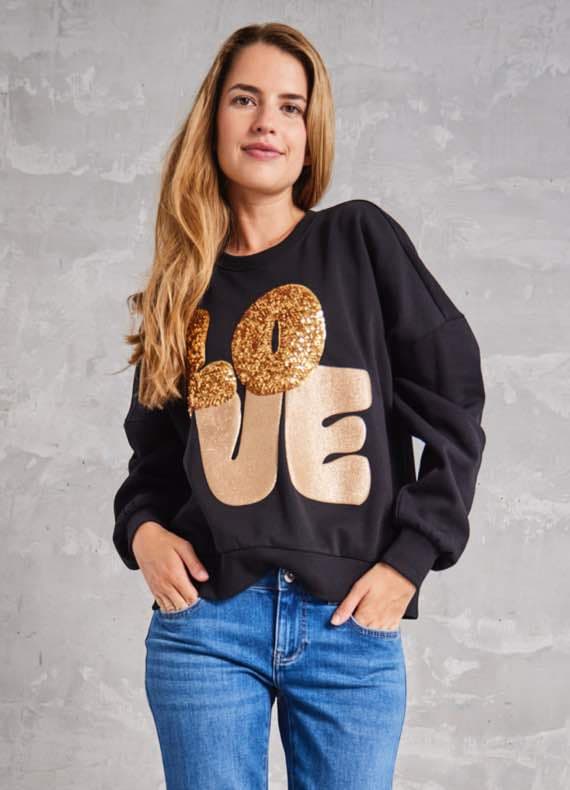 LOVE-Schriftzug auf schwarzem Pullover – Frau mit langen blonden Haaren trägt Pullover und blaue Jeans