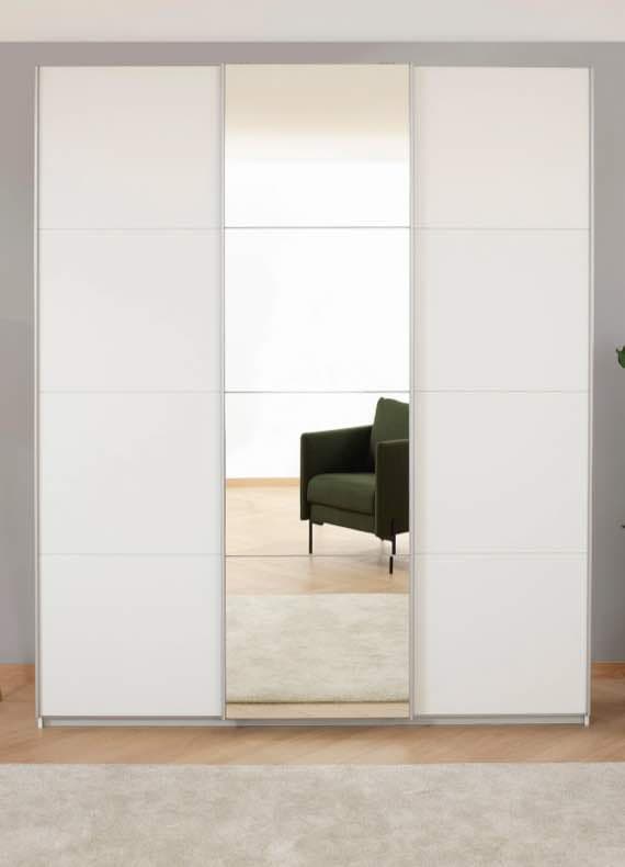 Weißer Schrank mit Spiegeltür, im Hintergrund grüner Sessel und Zimmerpflanze.