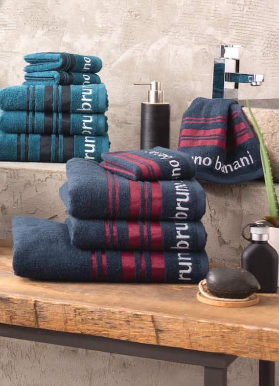 Gestapelte Handtücher mit Bruno Banani Schriftzug in Blau und Rot, Waschbecken und Seifenspender im Hintergrund